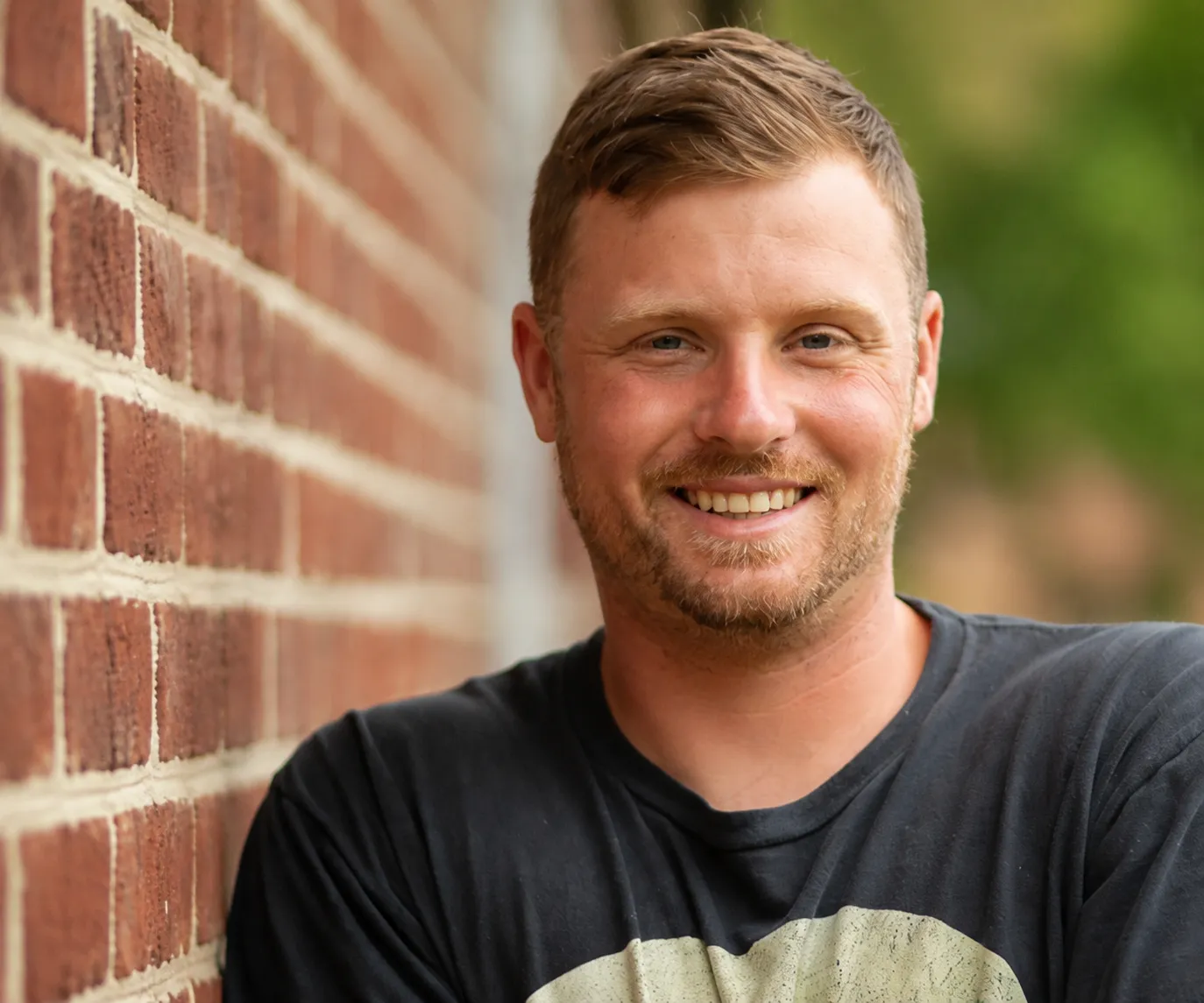 Drew smiling beside a brick wall